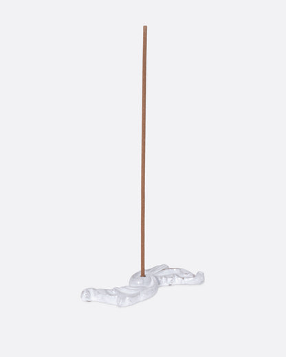 A white ceramic floral shaped incense burner, shown from the side with an incense stick in it.