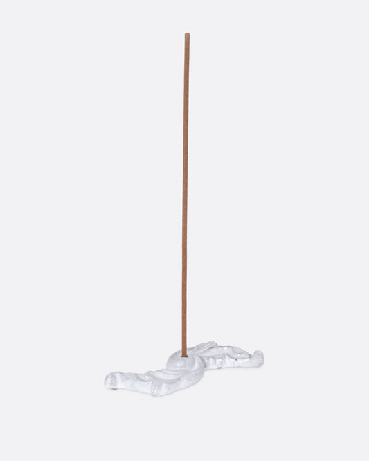 A white ceramic floral shaped incense burner, shown from the side with an incense stick in it.