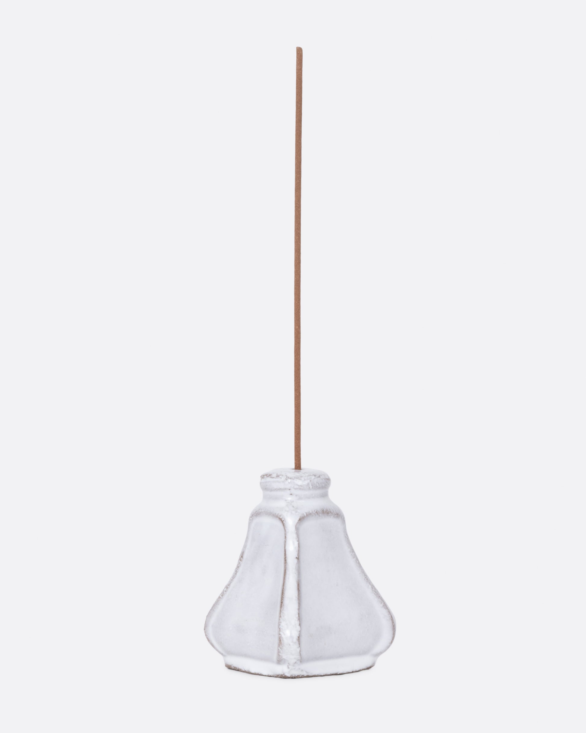 A white ceramic salt and pepper shaped incense burner with a stick in it, shown from the side.