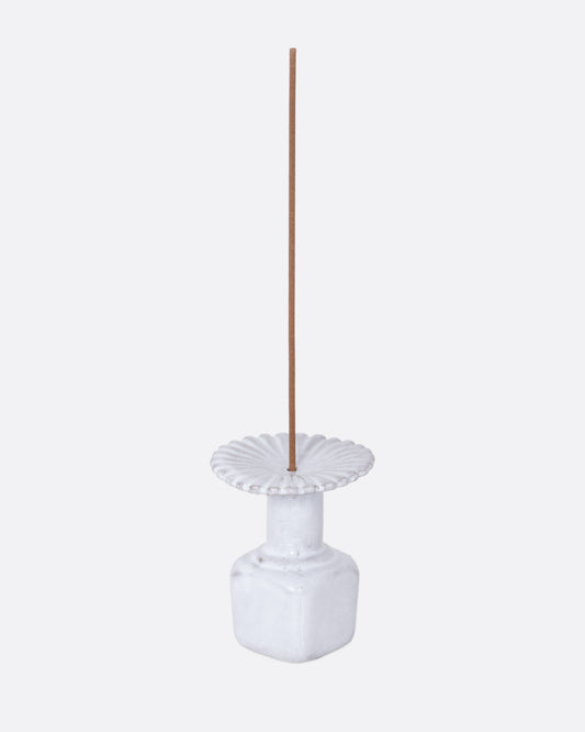  A white ceramic fluted incense holder, shown from the side with an incense stick in it.