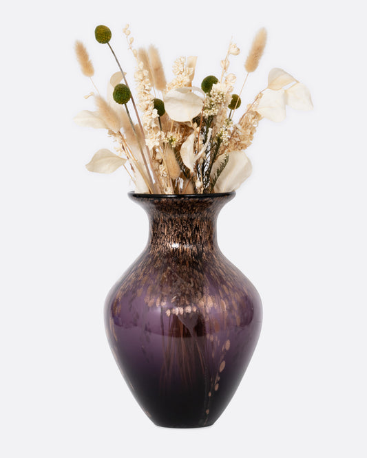 A black, purple, and gold glass vase with an arrangement of dried flowers. Shown from the front.