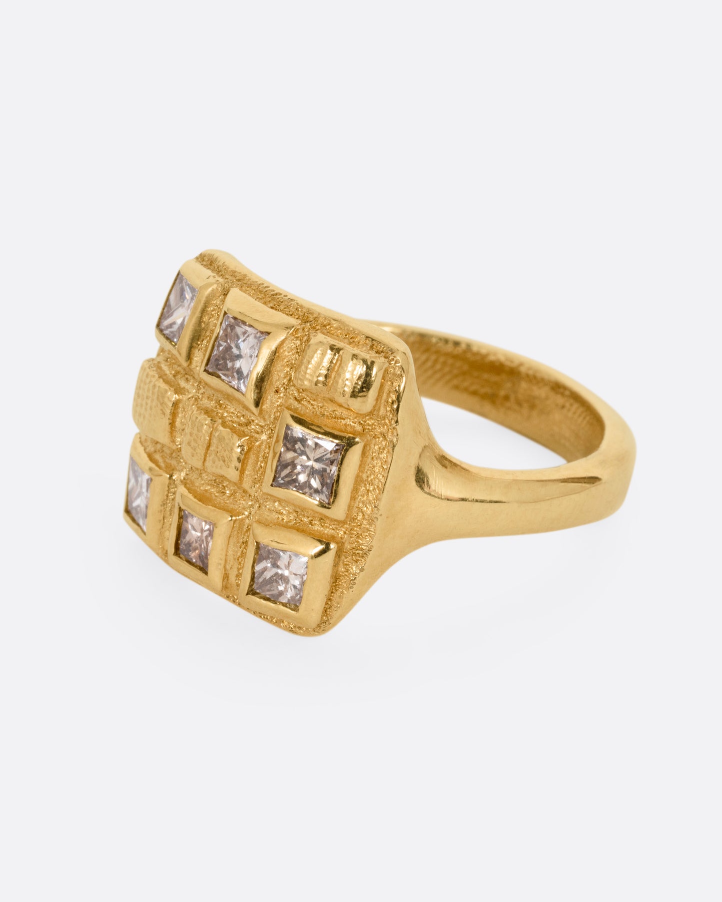 A yellow gold ring with princess cut brown diamonds and raised textural squares across its broad face. Shown from the side.