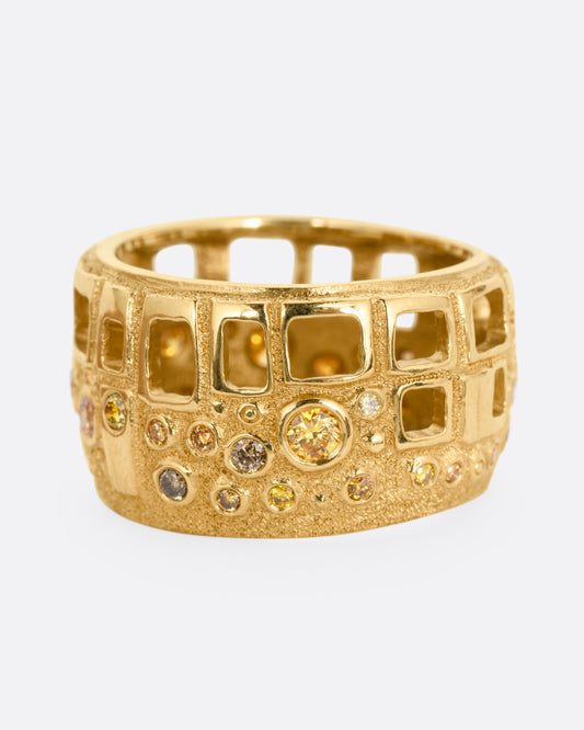A wide yellow gold cigar band with multicolored diamonds and open cutouts, shown from the front.