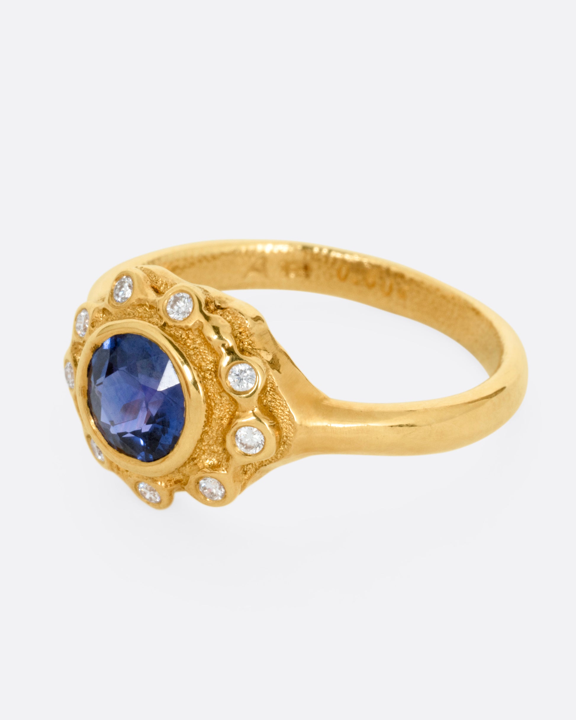 A yellow gold ring with a halo of white diamonds around a sapphire, shown from the side.
