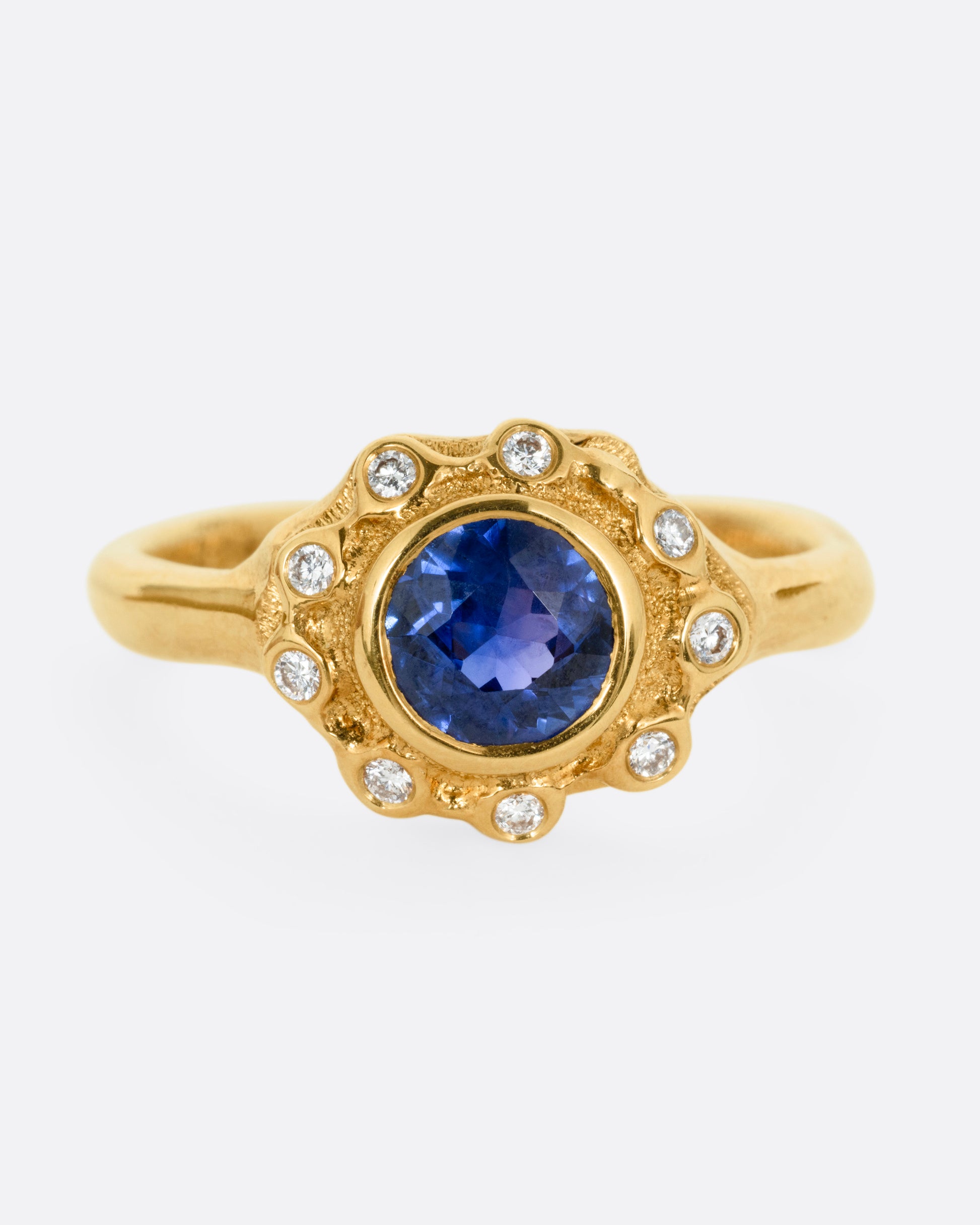 A yellow gold ring with a halo of white diamonds around a sapphire, shown from the front.