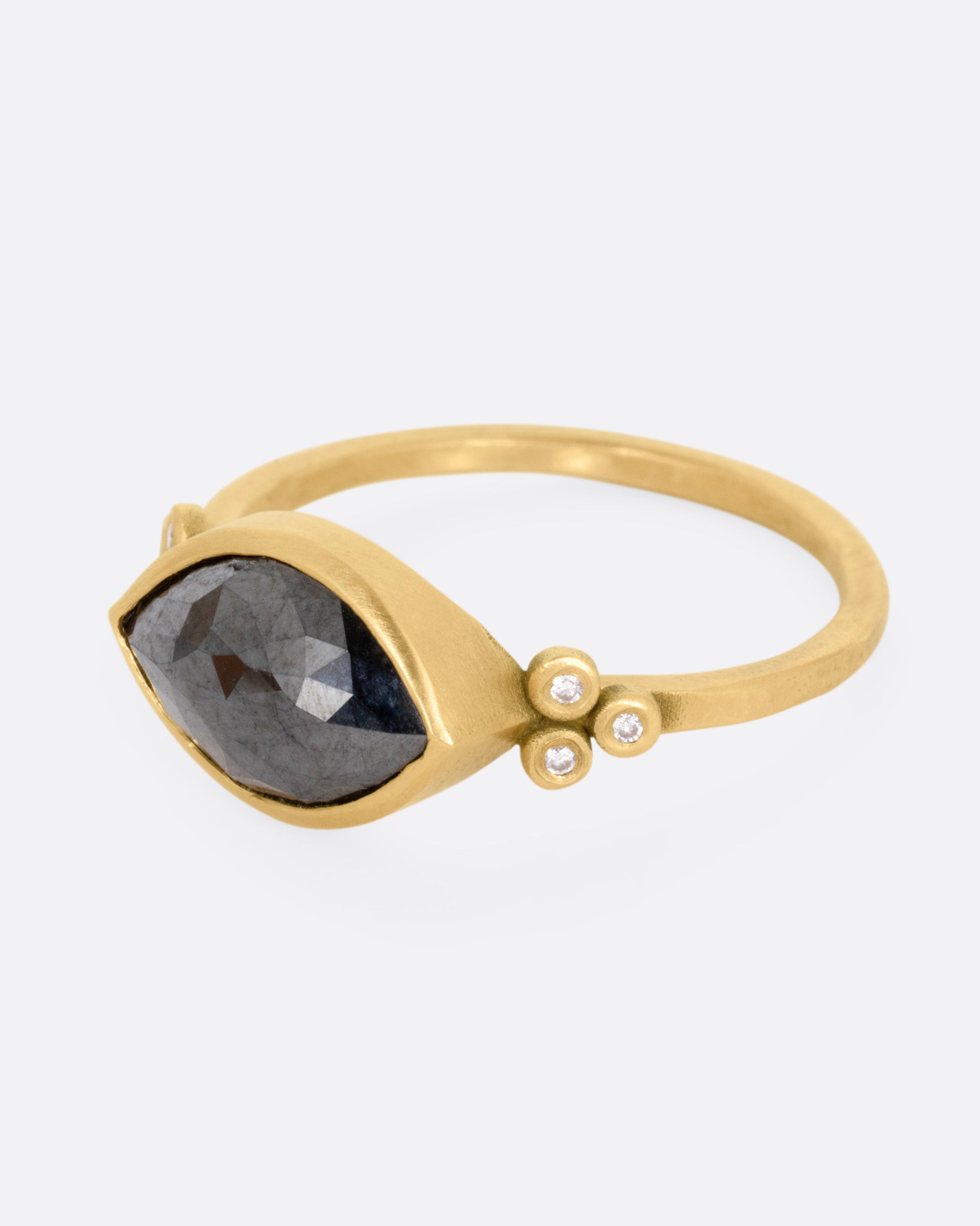 A yellow gold ring with a wide eye-shaped black marquise diamond flanked by a trio of white diamonds, shown from the side.