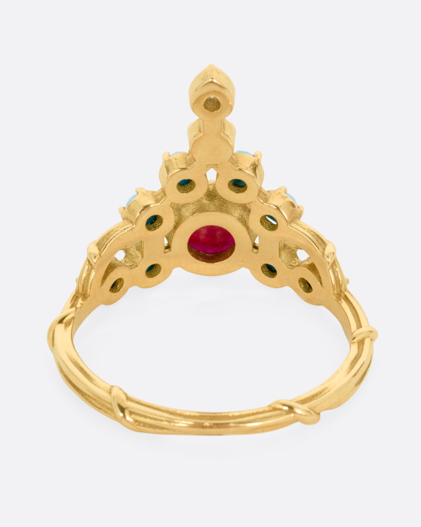 A yellow gold stacker ring with a ruby center surrounded by turquoise cabochons with a diamond tip, shown from the back.