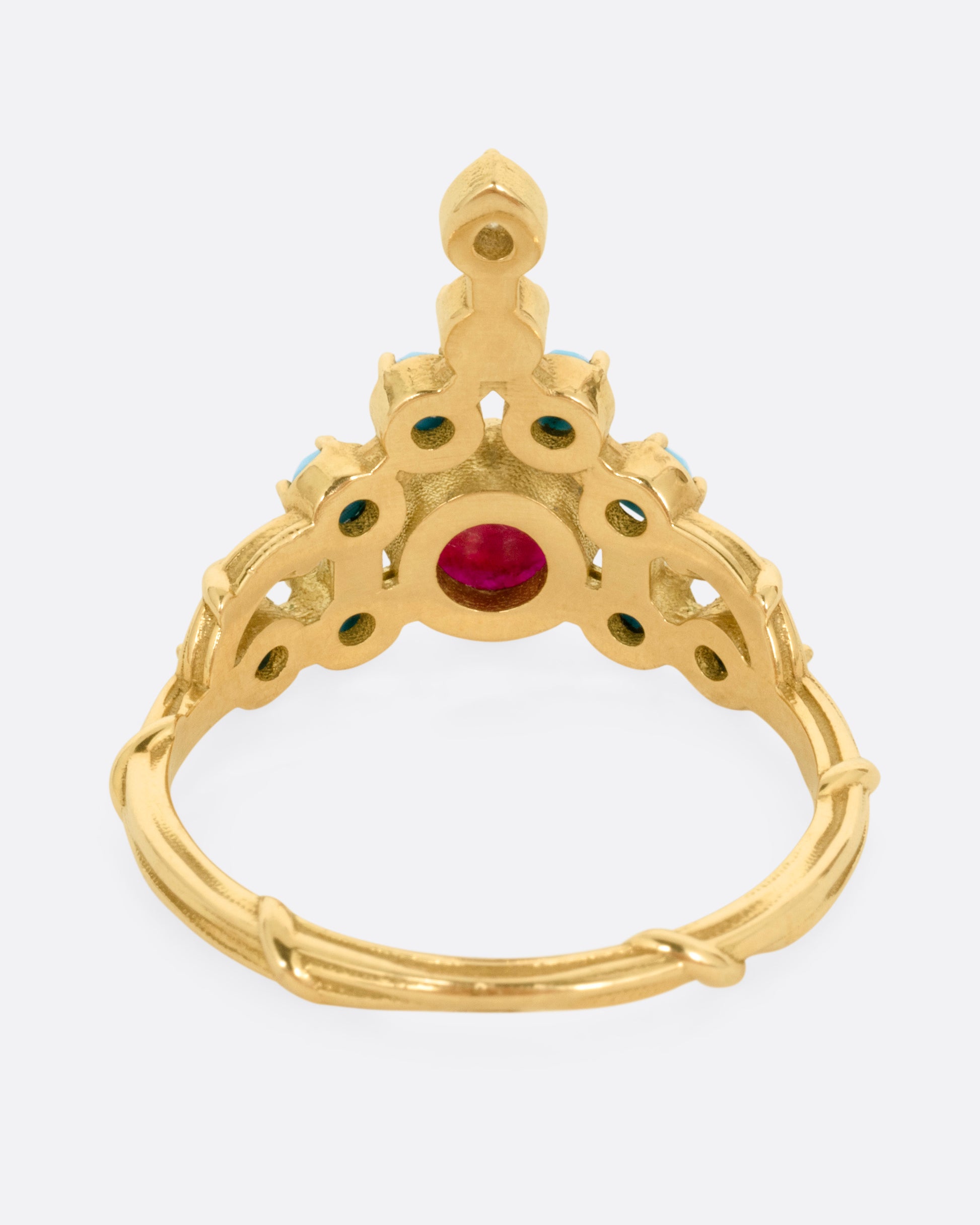 A yellow gold stacker ring with a ruby center surrounded by turquoise cabochons with a diamond tip, shown from the back.