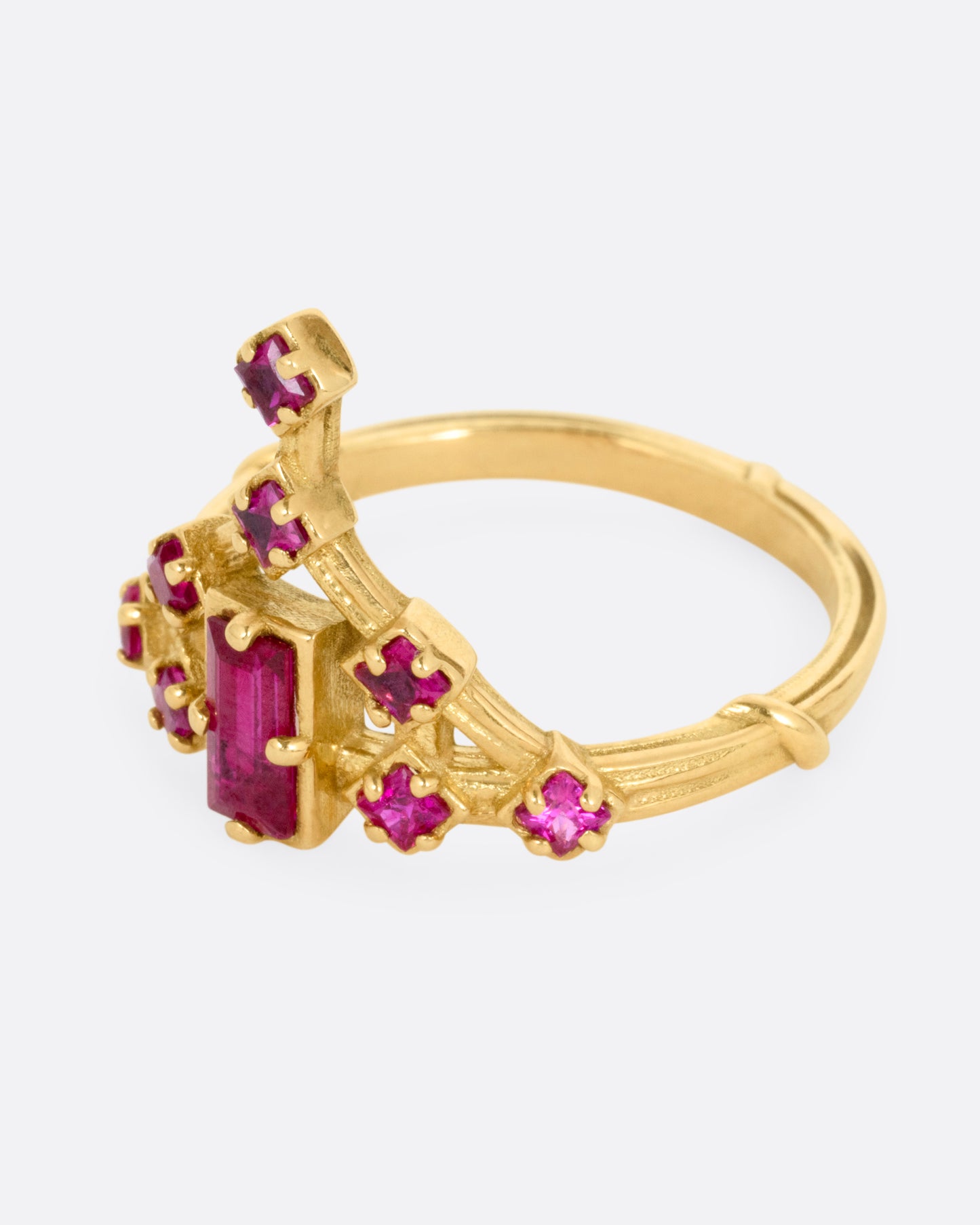 A yellow gold ring with a baguette ruby and princess cut ruby accents. Shown from the side.