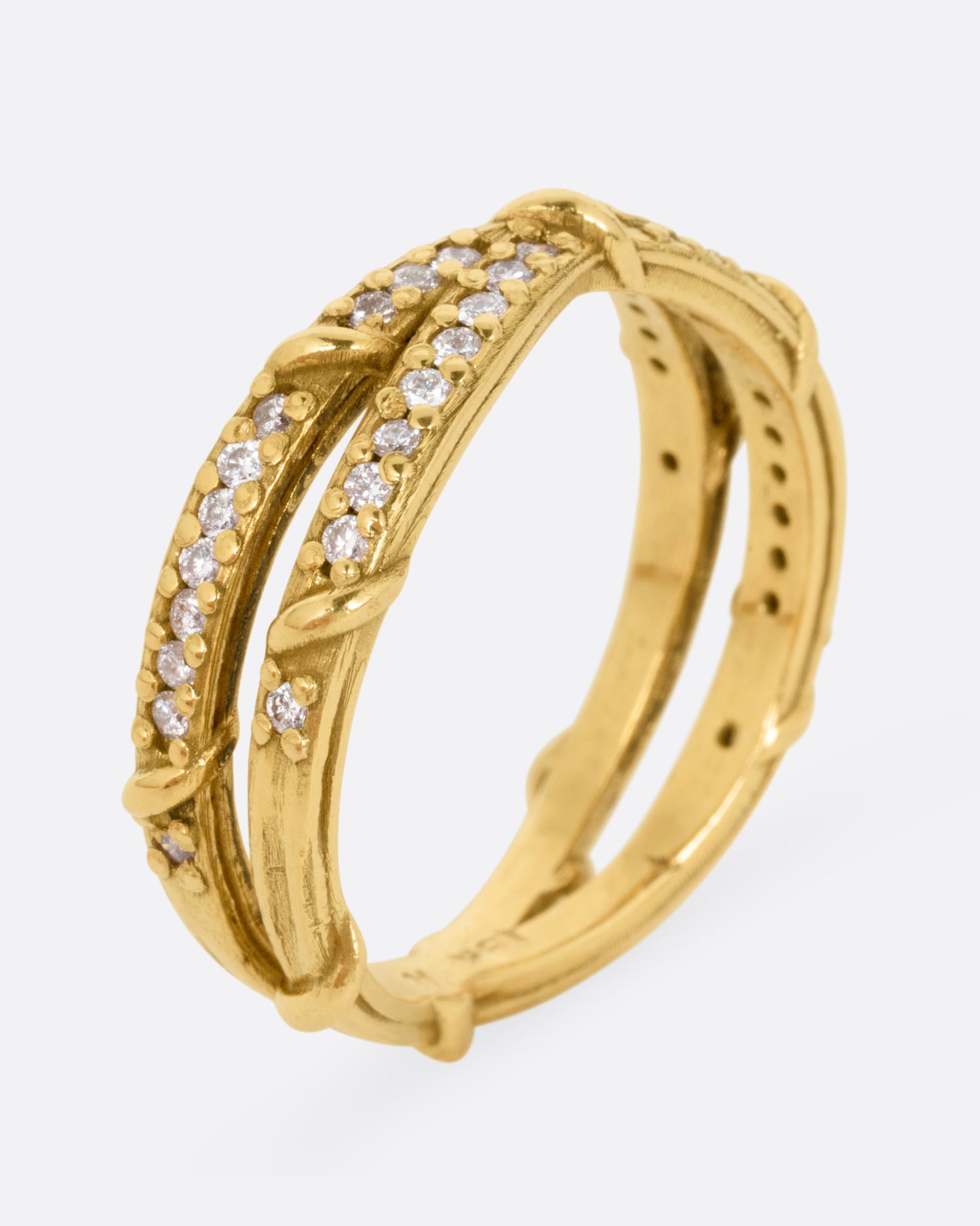 A yellow gold ring with two eternity bands intersecting at the middle and wrapped in vines and colorless diamonds. Shown standing up from the side.