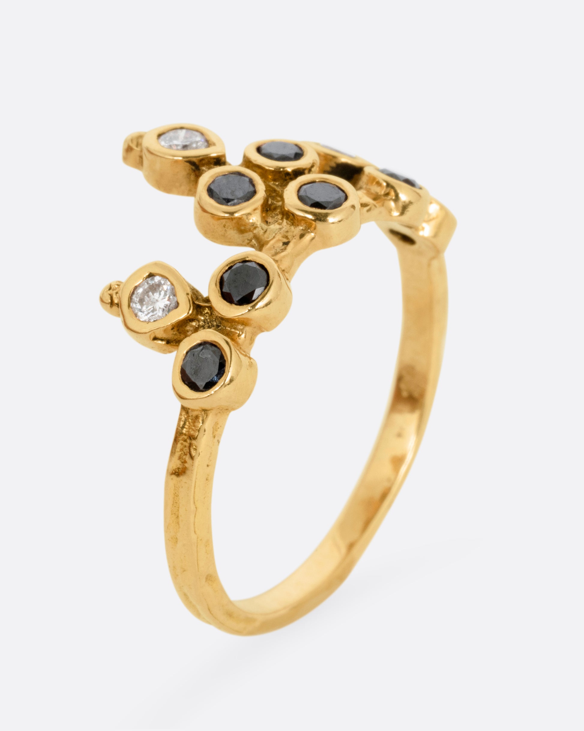 A yellow gold tiara ring with white and black diamonds, shown standing up from the side.
