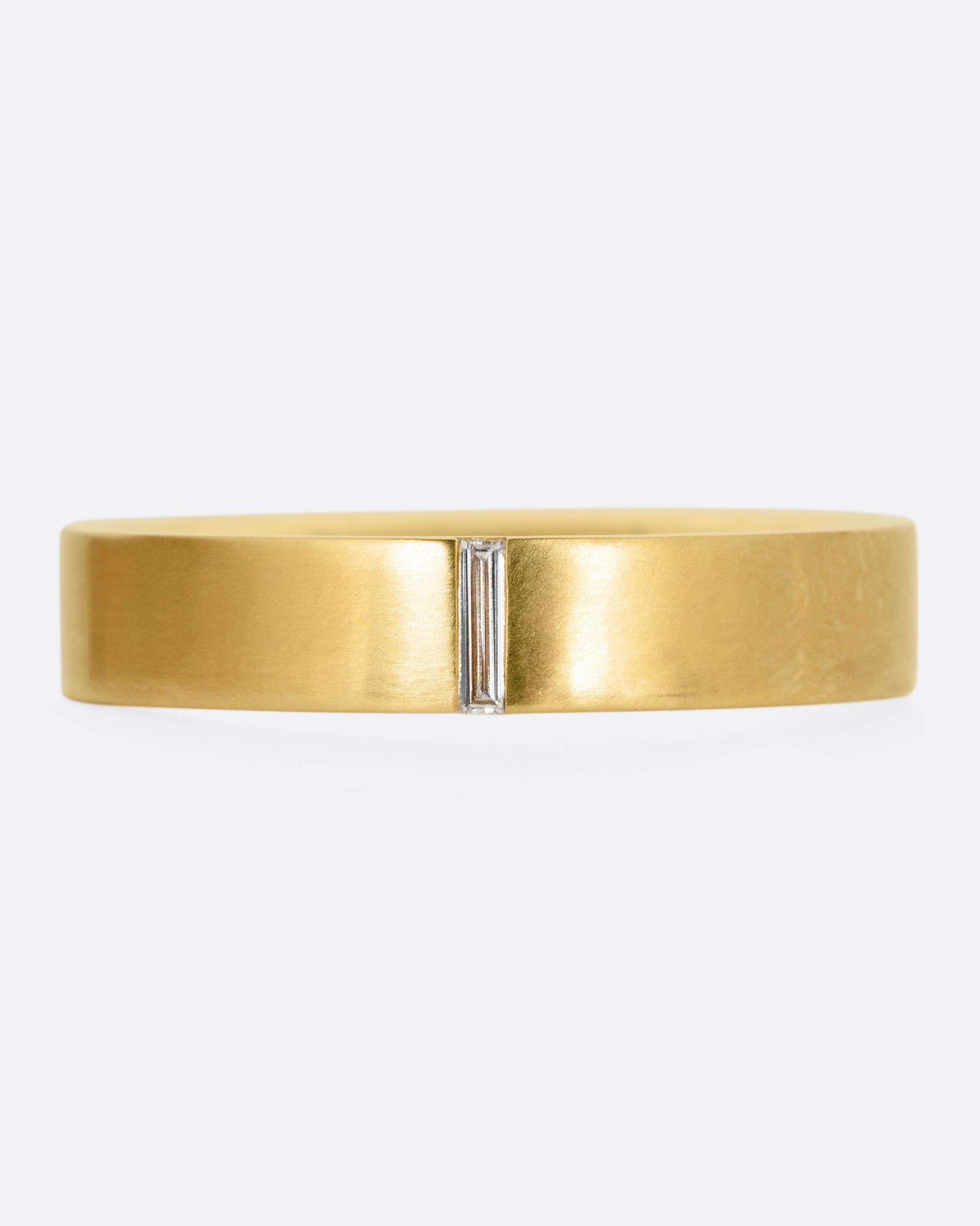 A yellow gold ring with a baguette diamond, shown from the front.