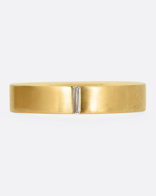 A yellow gold ring with a baguette diamond, shown from the front.