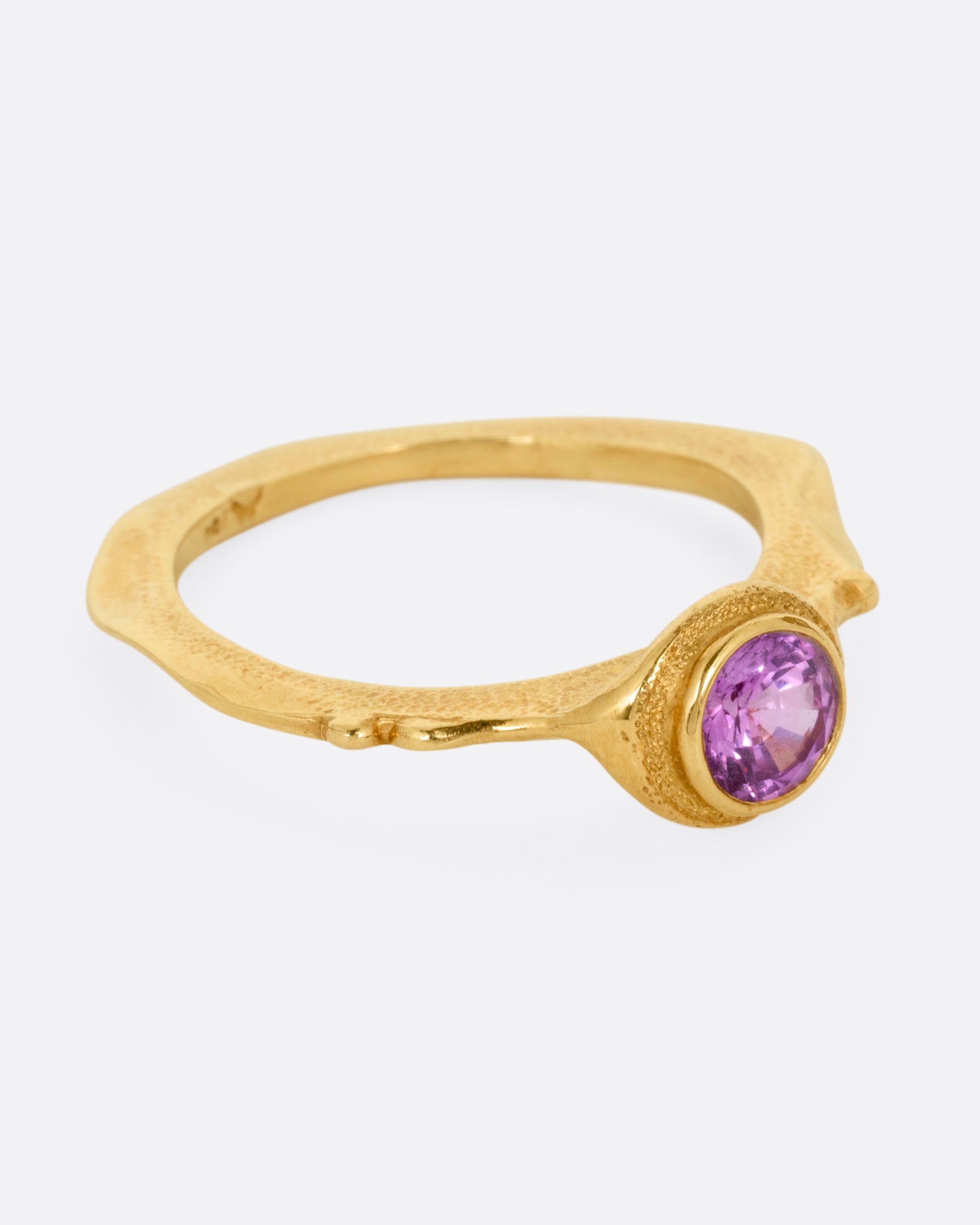 A yellow gold narrow sculptural ring with a purple sapphire, shown from the side.
