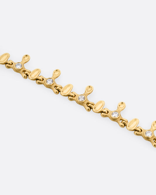 A yellow gold bracelet with a drippy pattern and white diamonds, shown from the front.