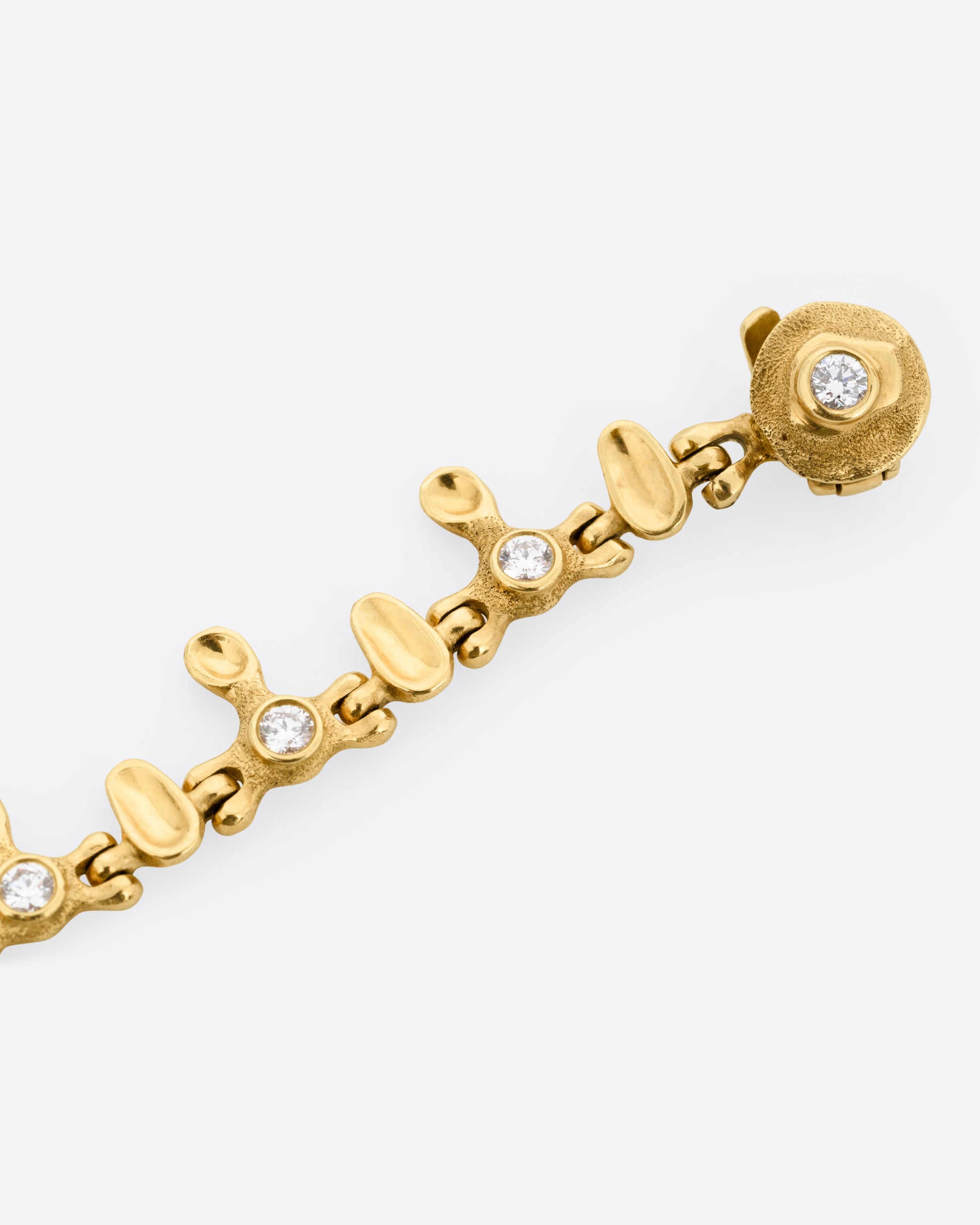 A yellow gold bracelet with a drippy pattern and round clasp with white diamonds, shown from the front.