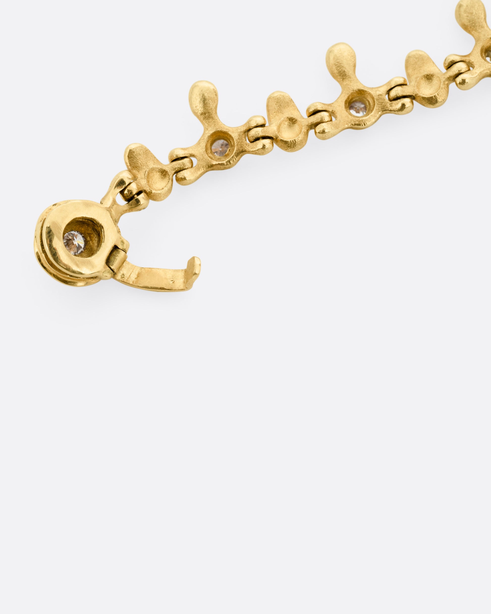 A close up of the clasp of a yellow gold bracelet with a drippy pattern and white diamonds, shown from the back.