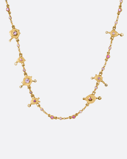 A yellow gold necklace with purple sapphires and diamonds set in handmade stations, shown from the front.