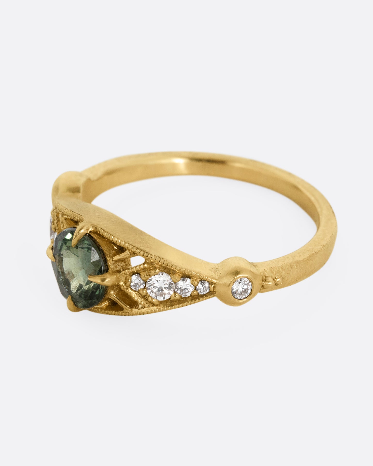 A yellow gold ring with a green Montana sapphire at the center and cutout details and white diamonds. Shown from the side.