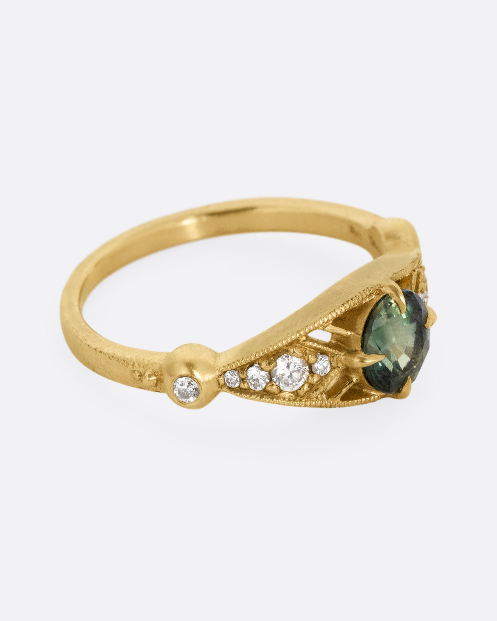 A yellow gold ring with a green Montana sapphire at the center and cutout details and white diamonds. Shown from the side.
