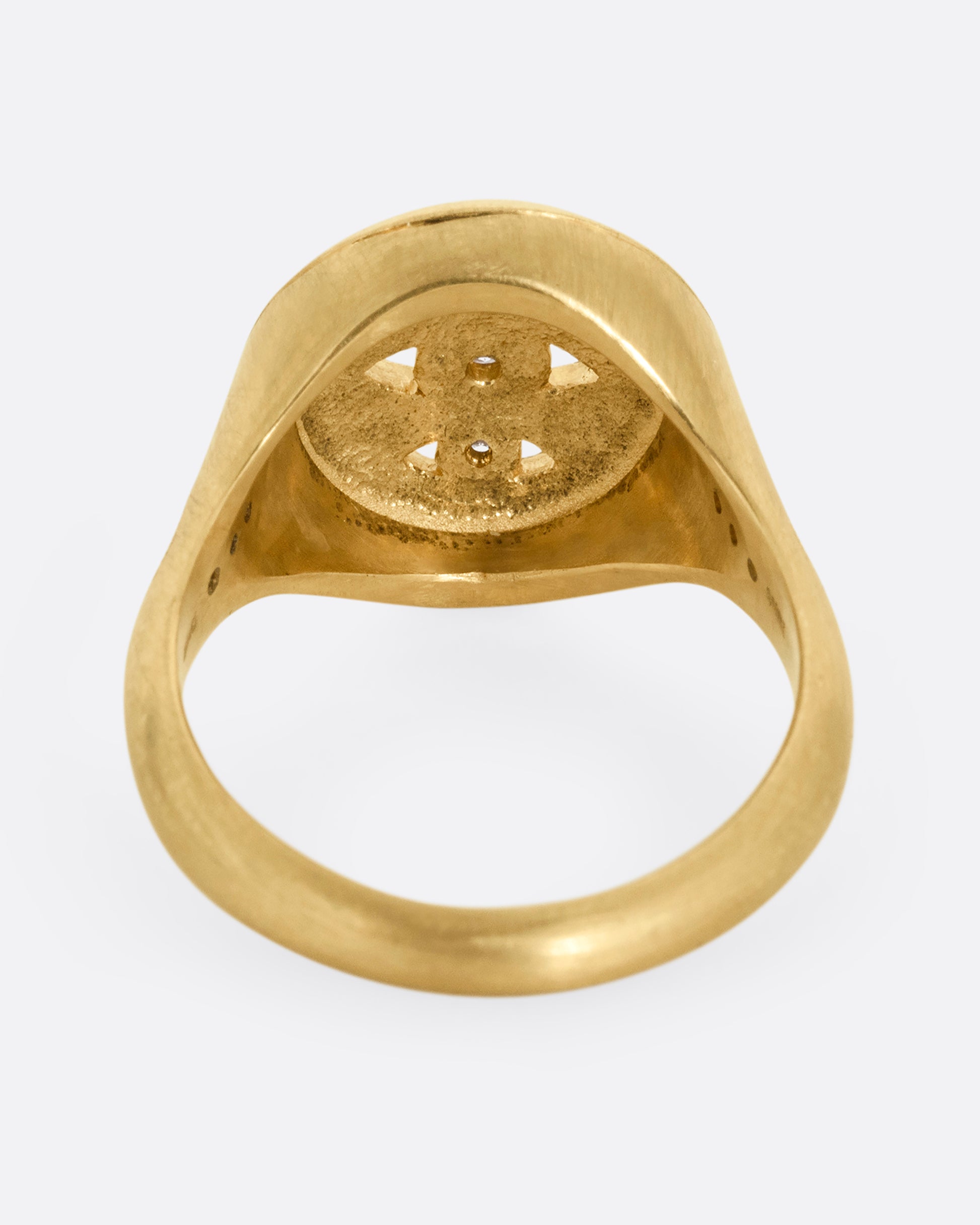 A yellow gold signet ring with three relief carved diamond eyes at the center. A trio of diamonds in teardrop shaped settings top each shoulder. Shown from the back.