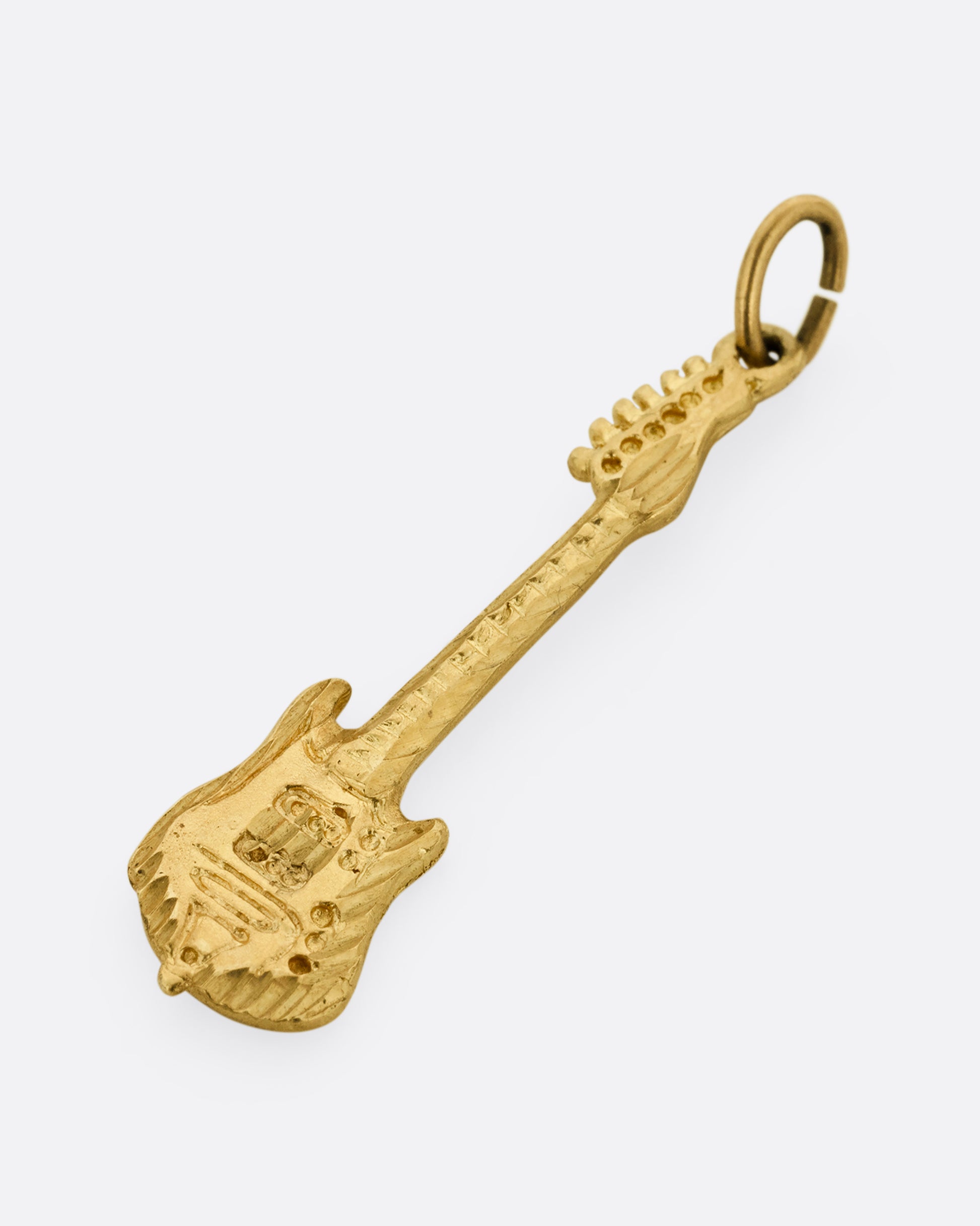 An electric guitar charm in yellow gold. Shown diagonally from the front lying flat.