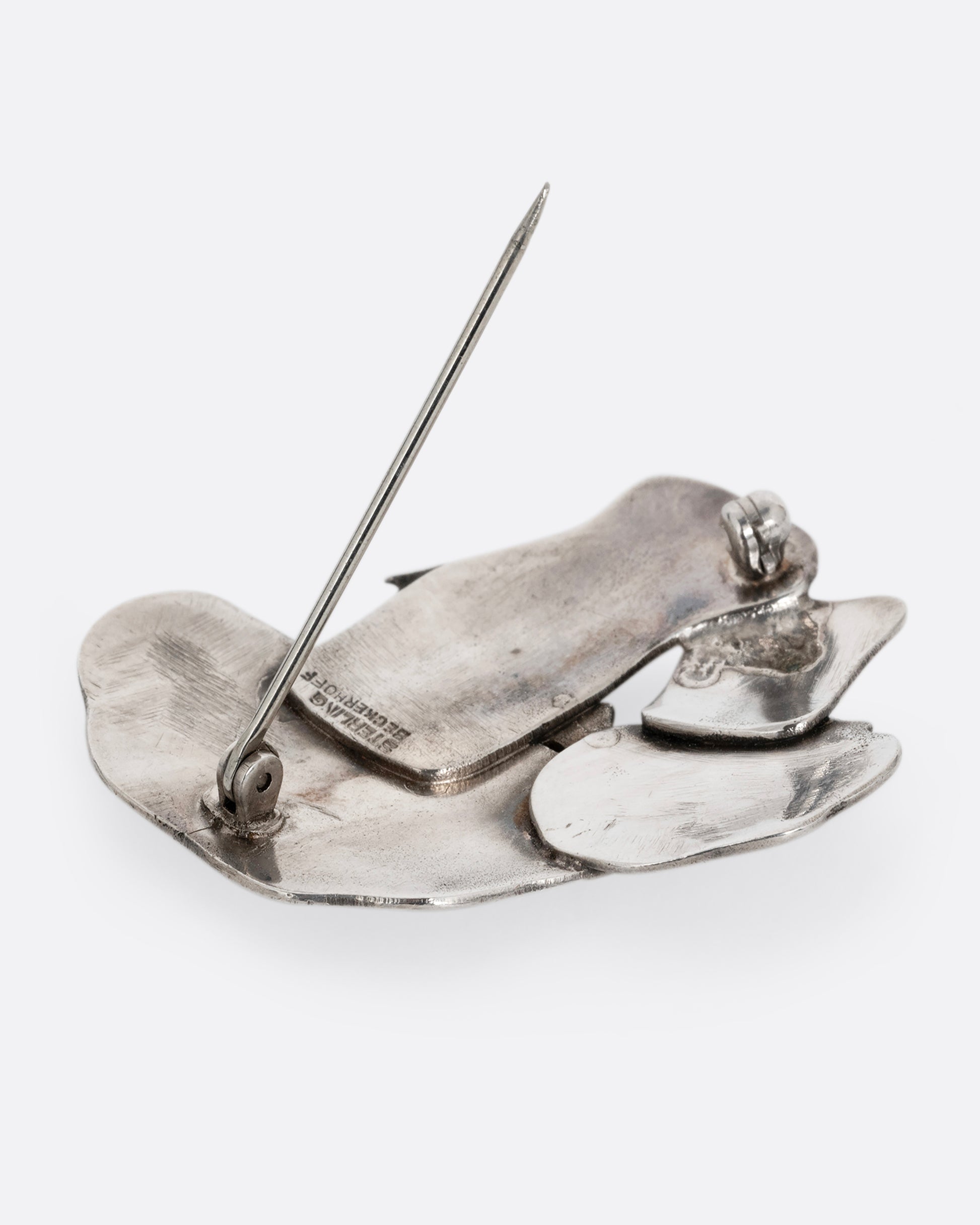 A silver pin with two mushrooms. Shown from the back.