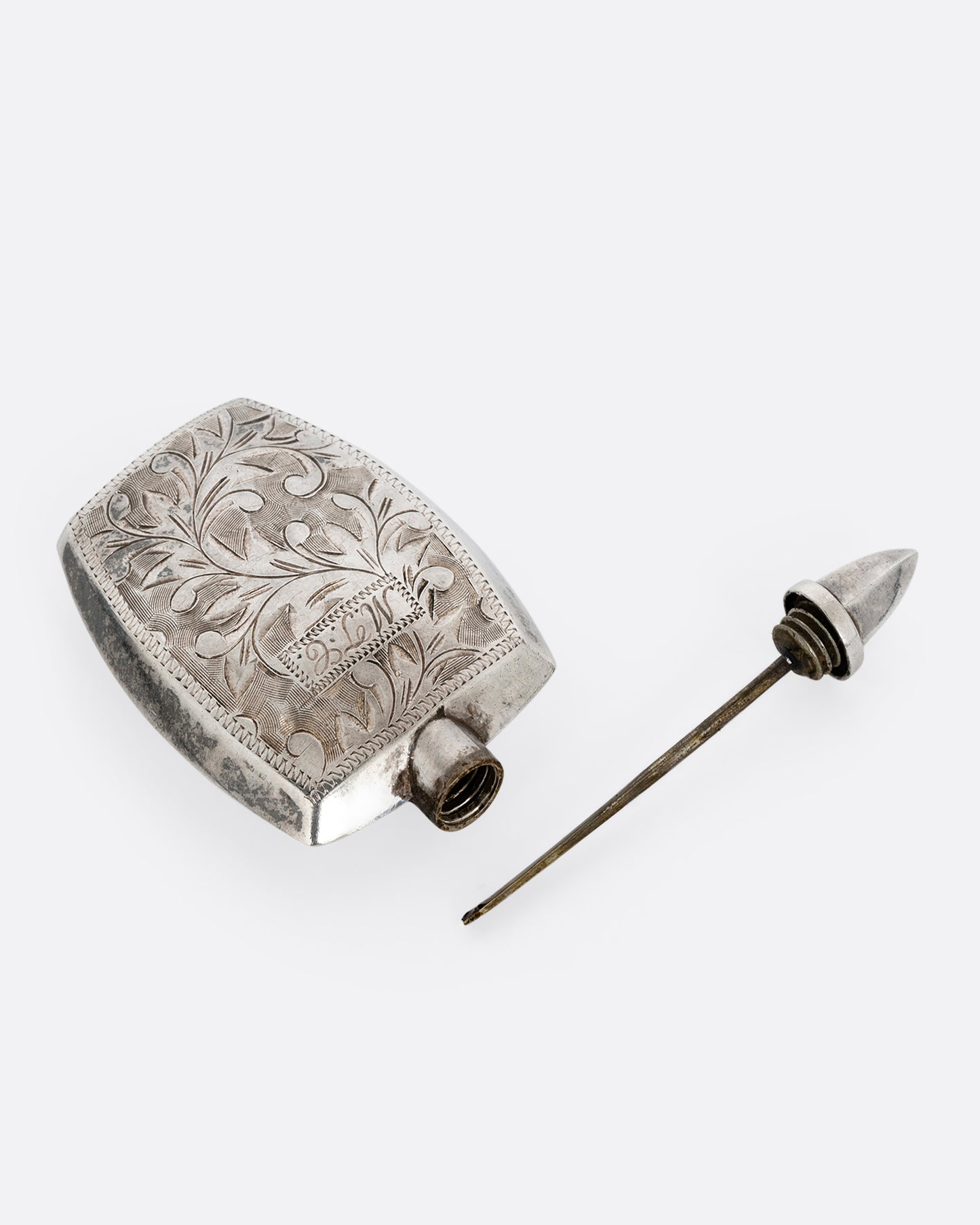 A silver perfume bottle with botanical etchings, a twist- off wand, and the engraved initials M.T.C. Shown open from the top.