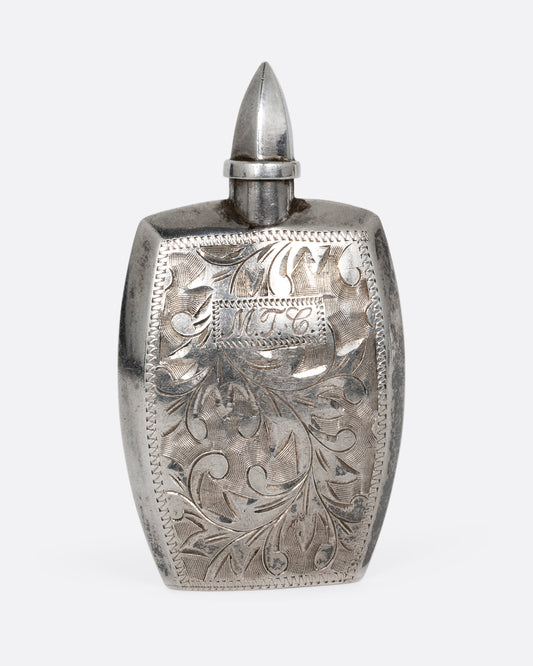 A silver perfume bottle with botanical etchings, a twist- off wand, and the engraved initials M.T.C. Shown from the front.