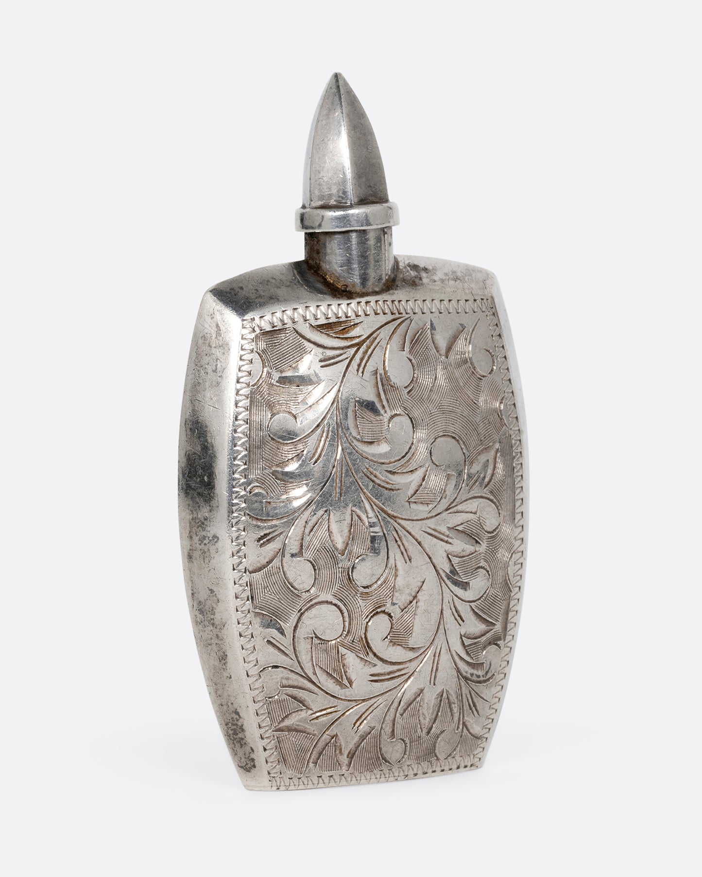 A silver perfume bottle with botanical etchings, a twist- off wand, and the engraved initials M.T.C. Shown from the back.
