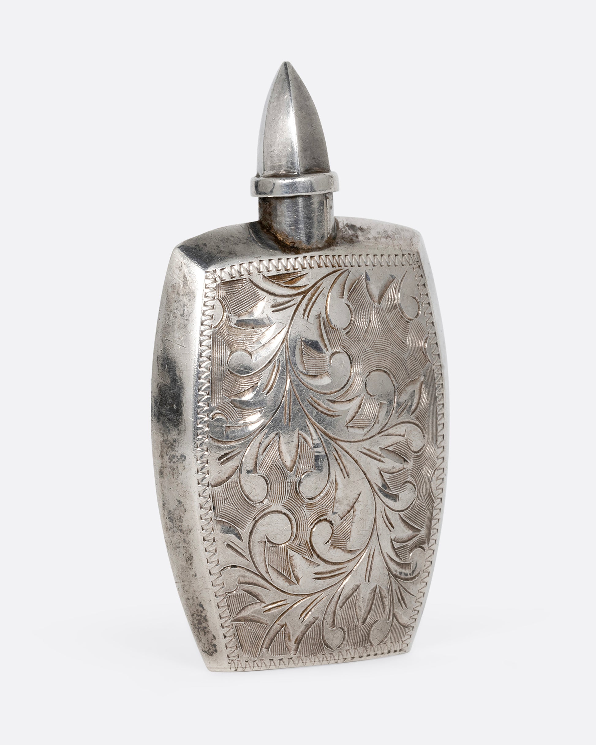 A silver perfume bottle with botanical etchings, a twist- off wand, and the engraved initials M.T.C. Shown from the back.