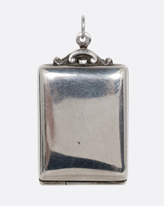 A silver rectangular locket with a filigreed top and hinged bottom. Shown from the front.