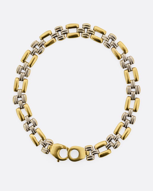 A bracelet with alternating silver and gold square links. Shown lying flat closed from the top. 