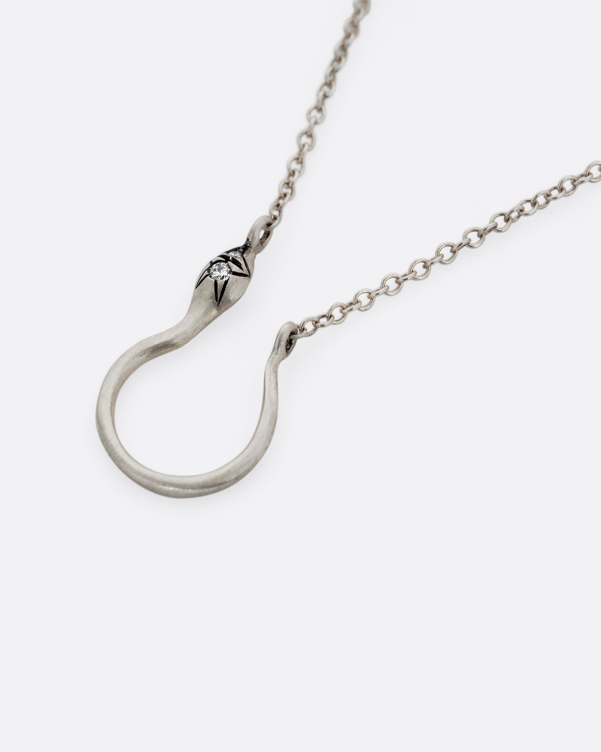 A silver snake shaped charm holder with diamonds on its face, hanging from a cable chain. Shown lying flat from the side.