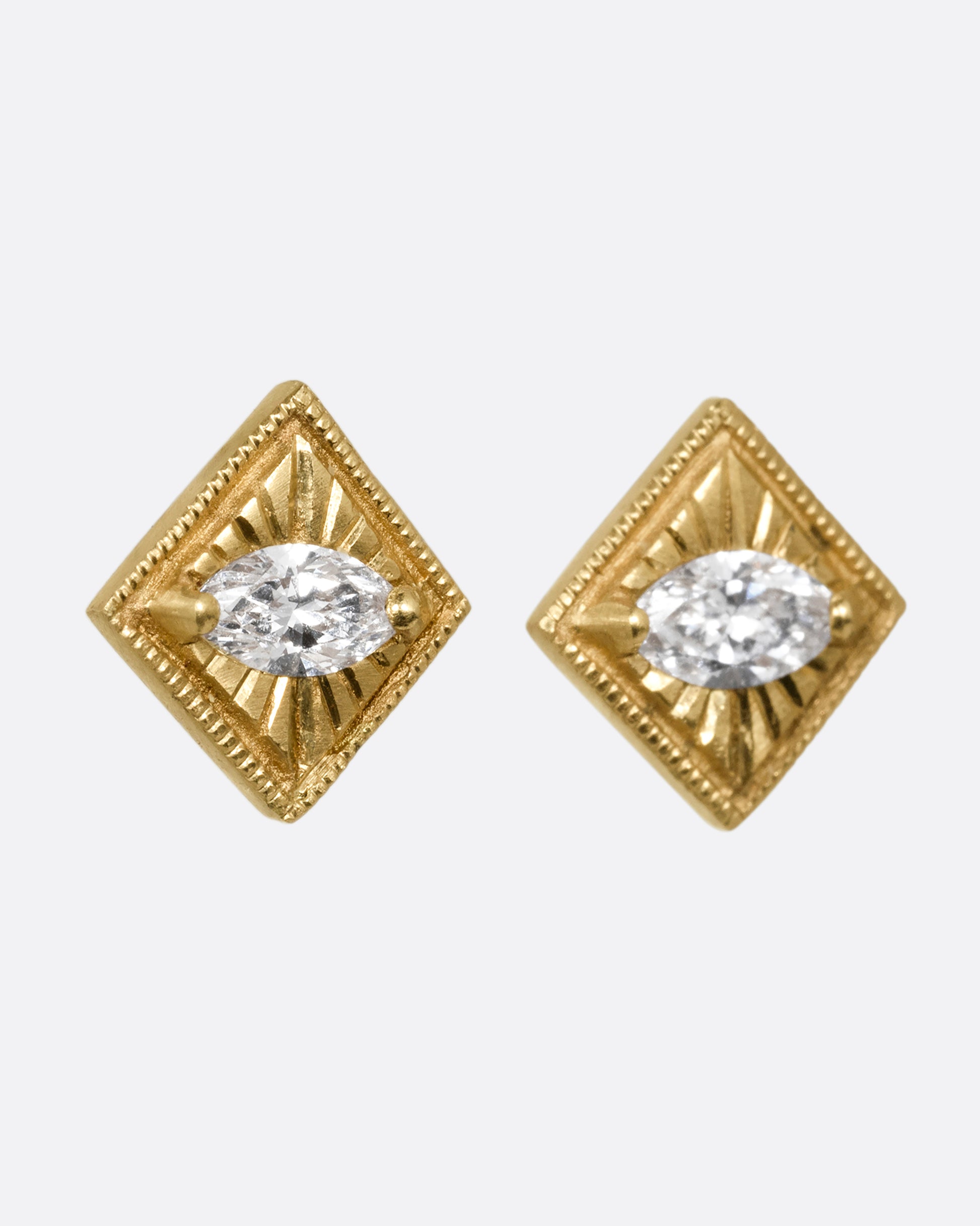 A pair of yellow gold square earrings with a milgrain border and marquis diamond in the center. Shown from the side.