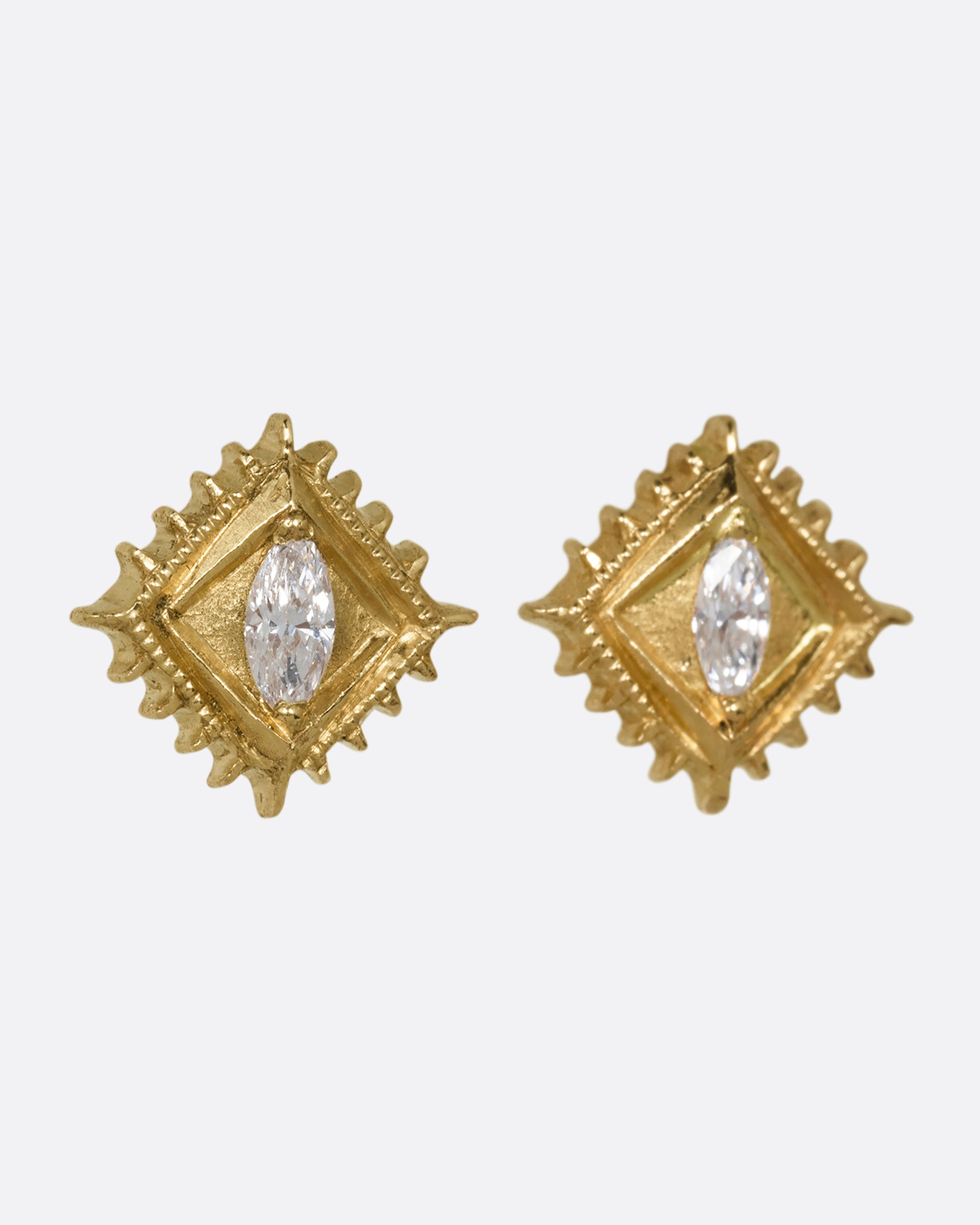 A pair of square yellow gold stud earrings with a milgrain border and white marquis diamond in the center. Shown on an angle from the front.