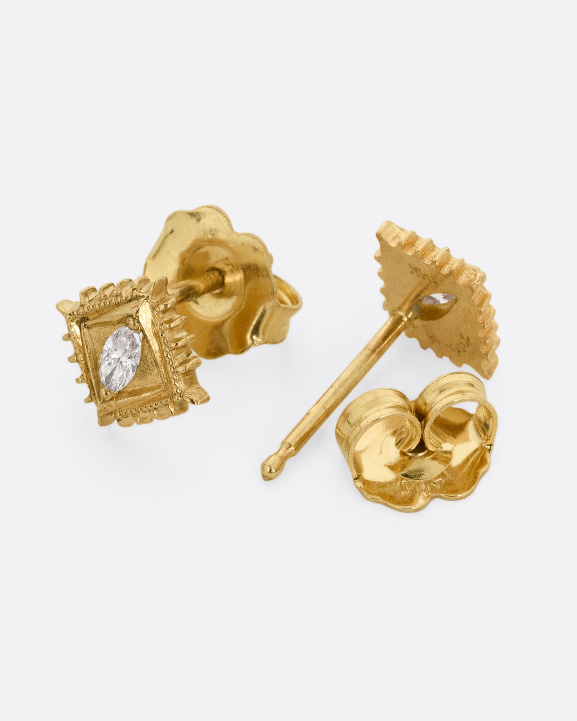 A pair of square yellow gold stud earrings with a milgrain border and white marquis diamond in the center. One earring is shown diagonally from the front and one is shown diagonally from the back with an open stud back.