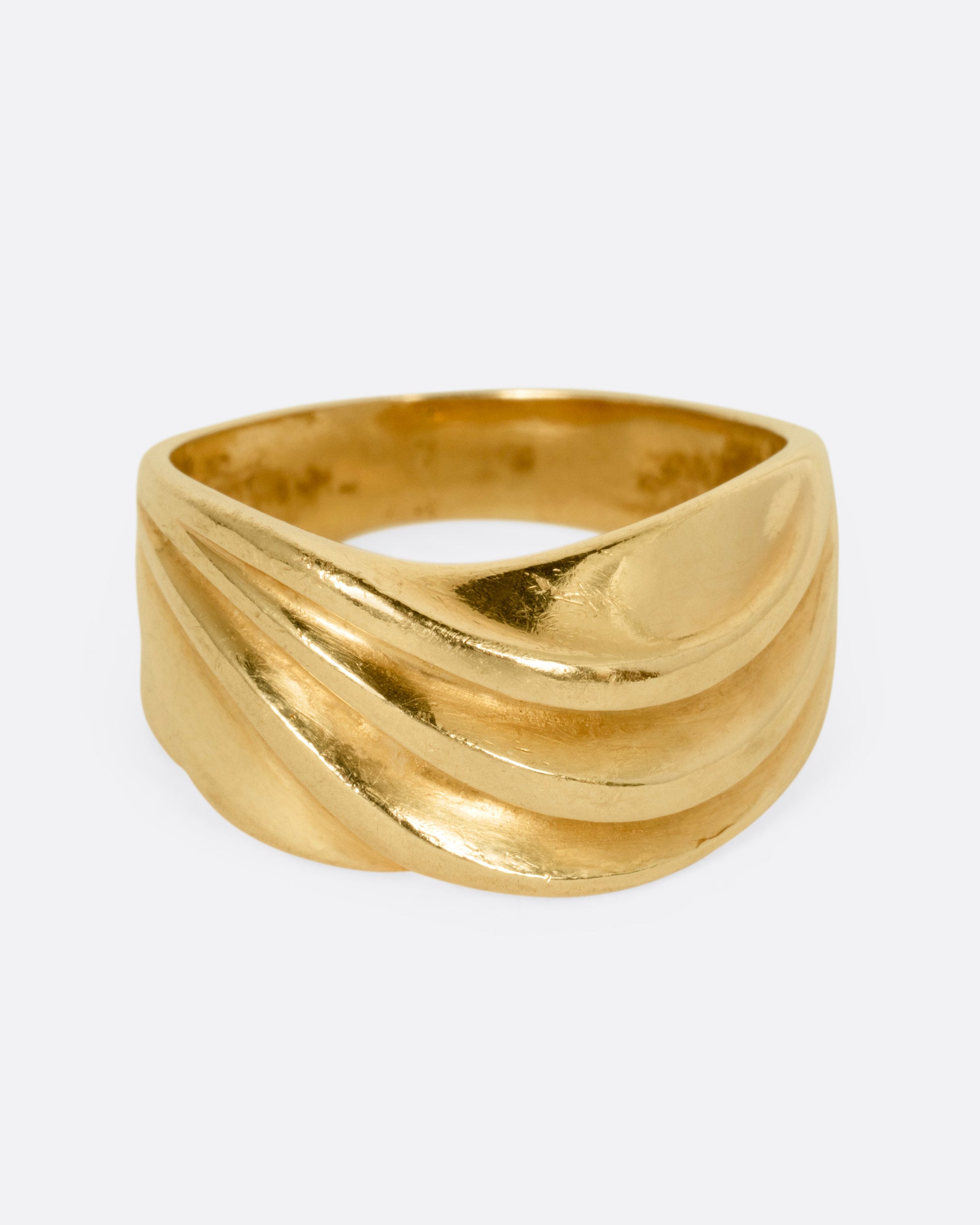A wide sculptural yellow gold ring, with dimensional waves across its face. Shown from the front.