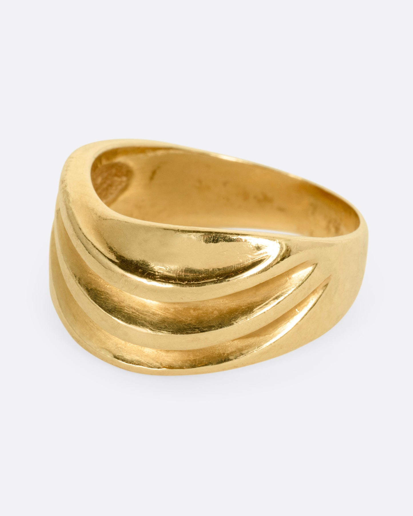 A wide sculptural yellow gold ring, with dimensional waves across its face. Shown from the side.
