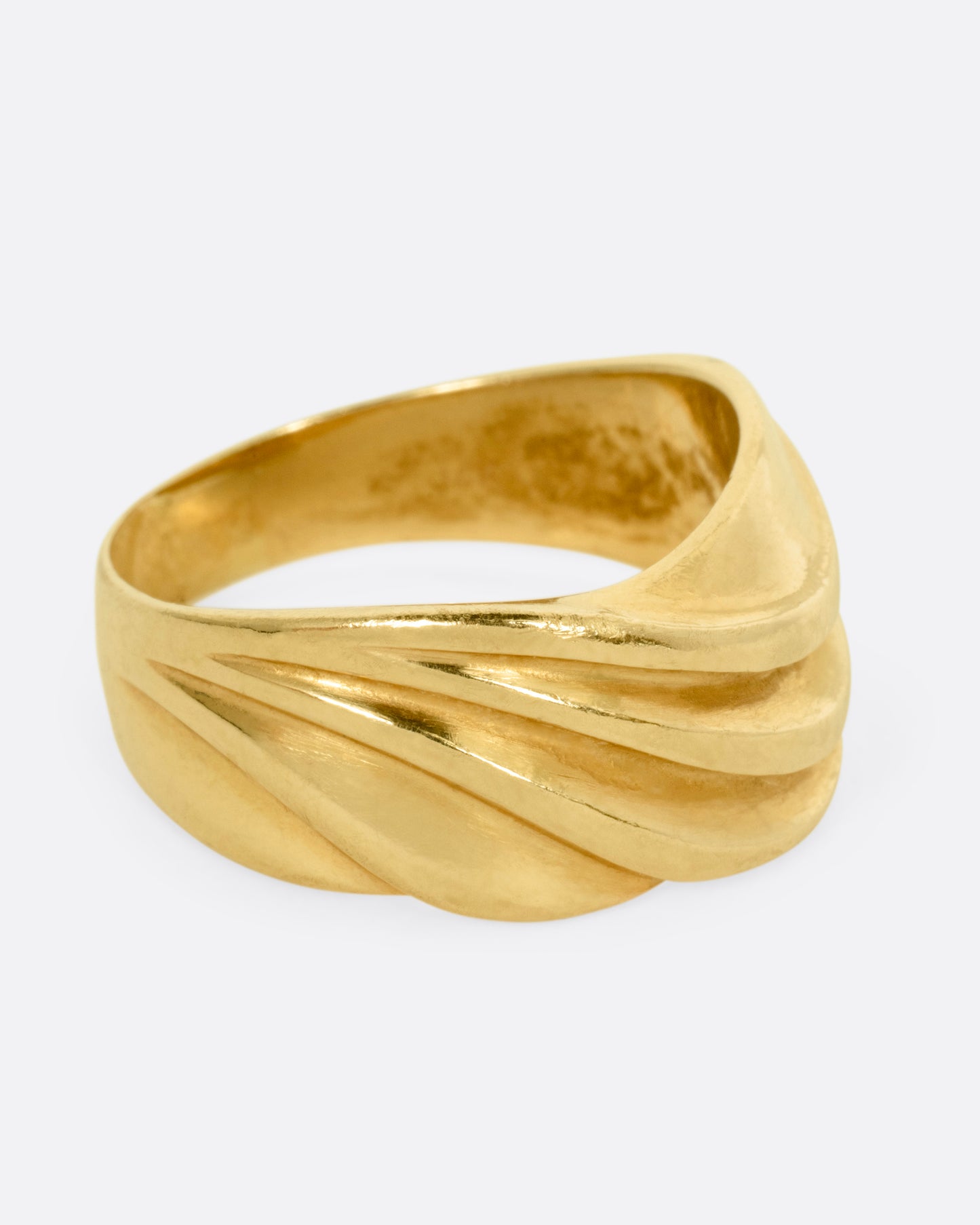 A wide sculptural yellow gold ring, with dimensional waves across its face. Shown from the side.