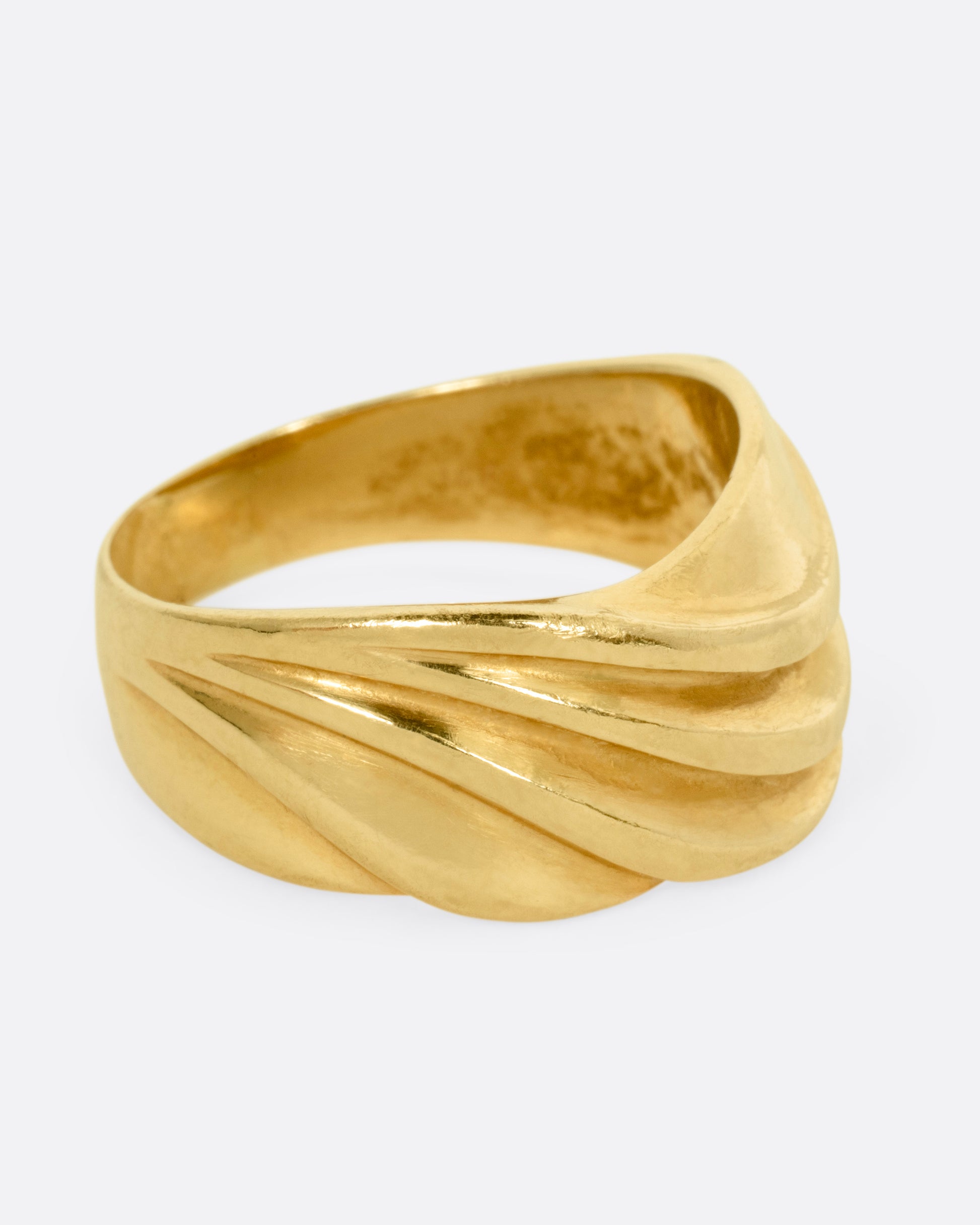 A wide sculptural yellow gold ring, with dimensional waves across its face. Shown from the side.