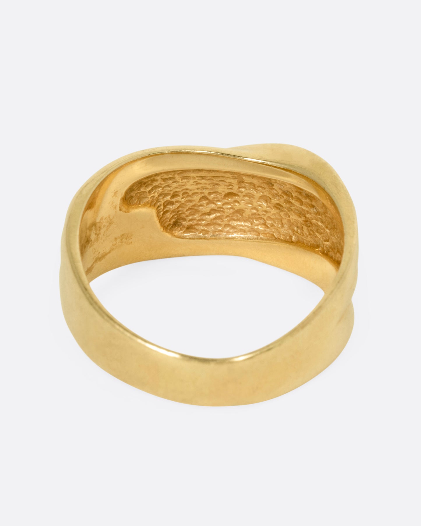 A wide sculptural yellow gold ring, with dimensional waves across its face. Shown from the back.