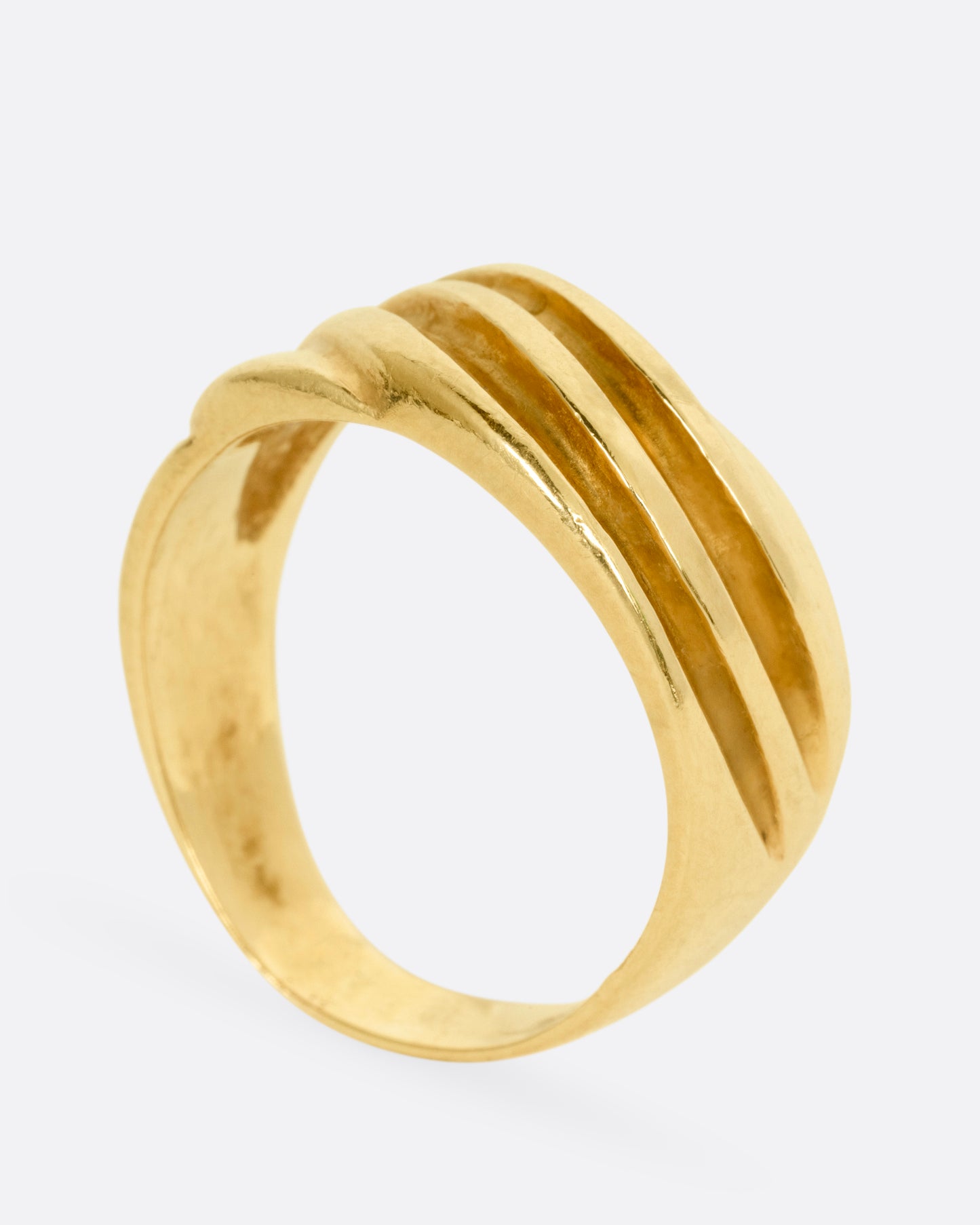 A wide sculptural yellow gold ring, with dimensional waves across its face. Shown from the side standing up.