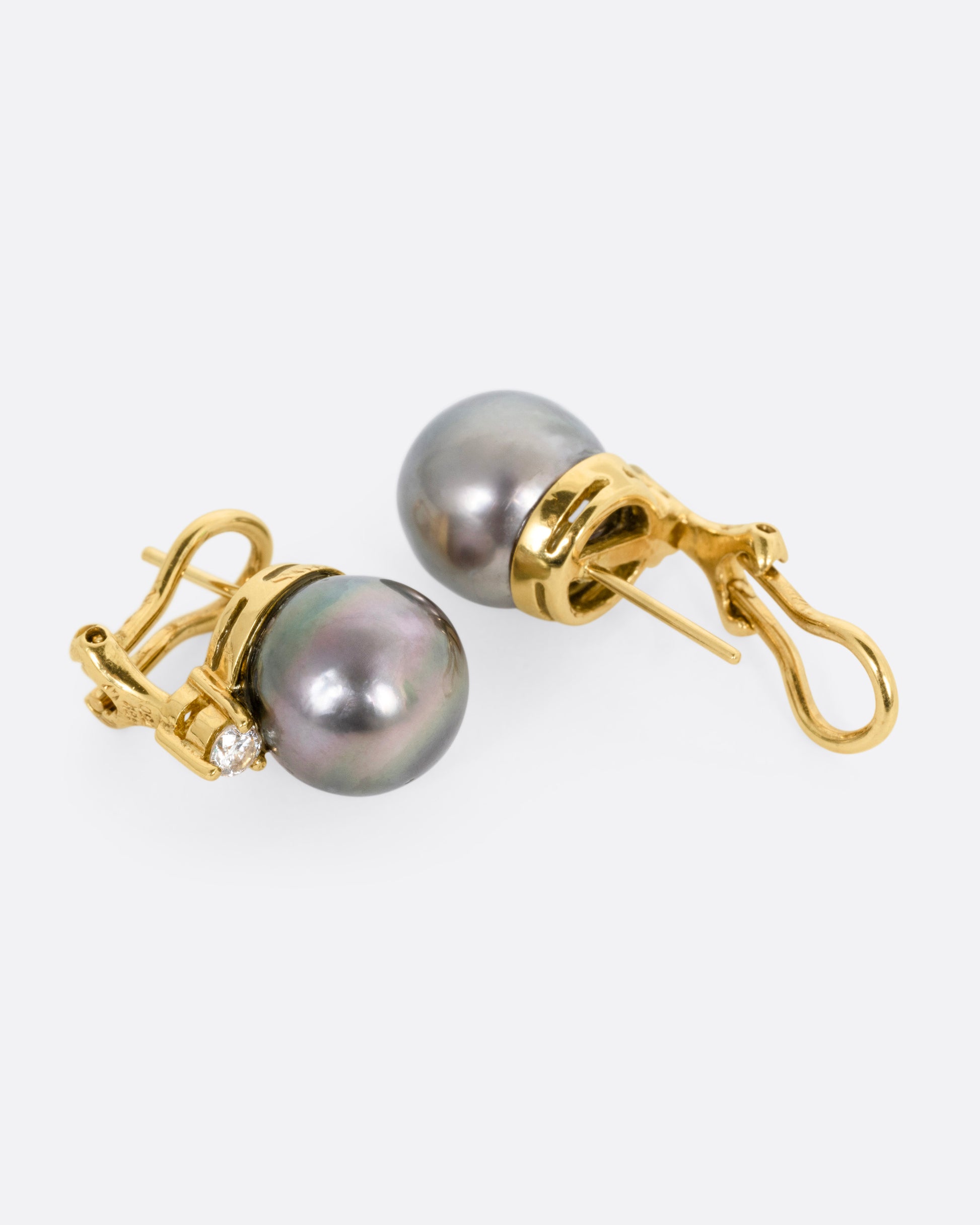A yellow gold earring with a black pearl, and a white diamond, shown lying on their sides, with one earring open.