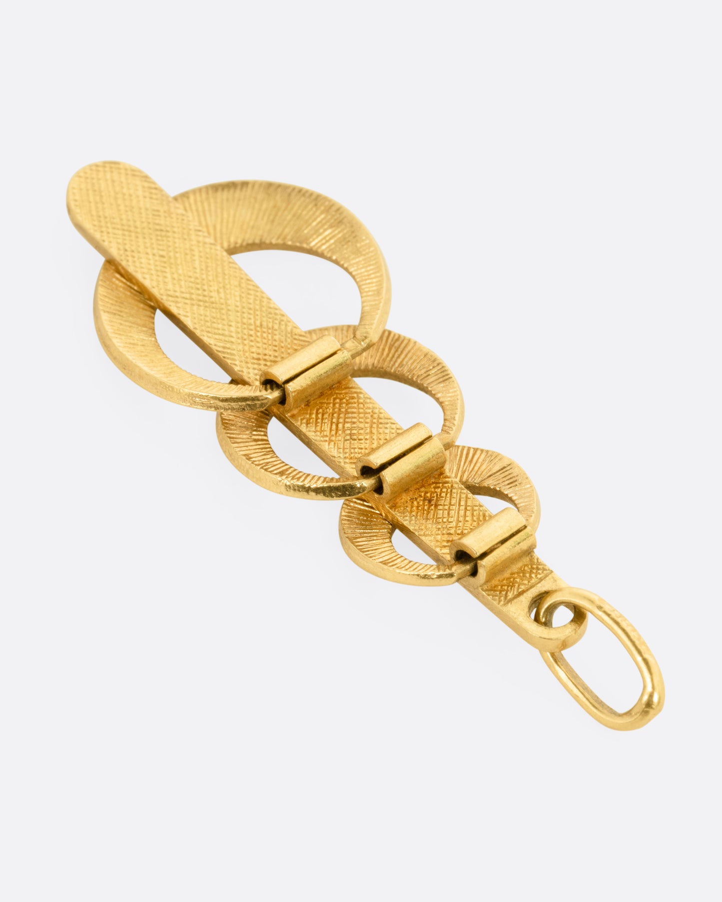 A yellow gold pendant with  three enamel crescents in blue and green on a red enamel bar. Shown from the back.