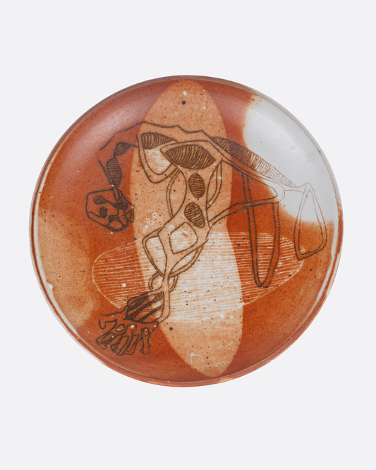 A ceramic plate with a hand painted abstract figure and an umber and white wash of color. Shown from the top.