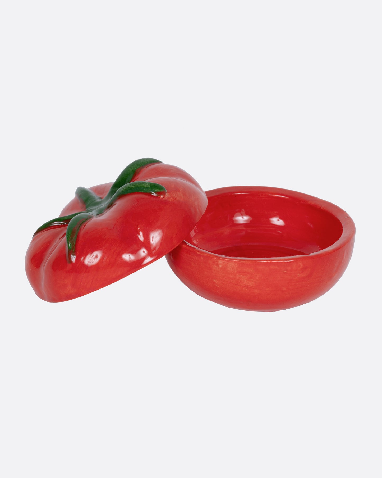 A tomato shaped salt cellar, shown from the front with the top leaning against its side.