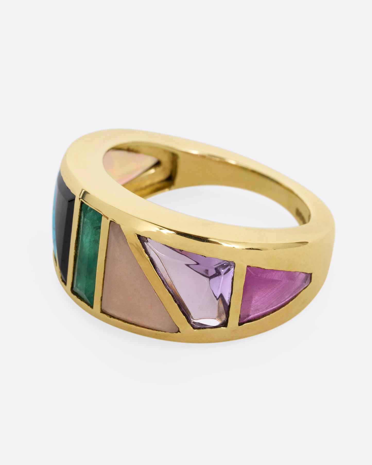 A yellow gold band with an array of gemstones in angular shapes. Shown from the side.