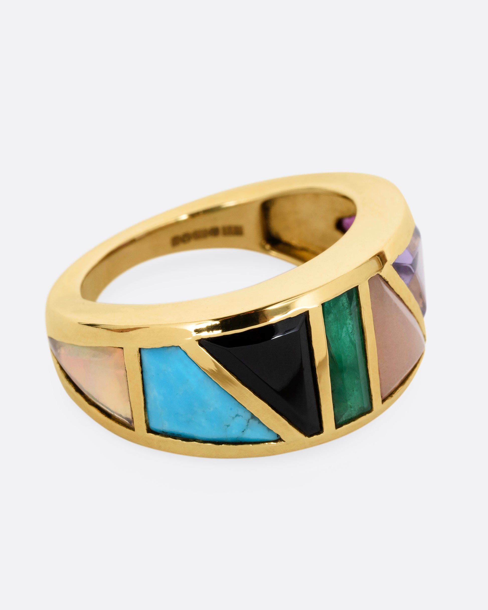 A yellow gold band with an array of gemstones in angular shapes. Shown from the side.