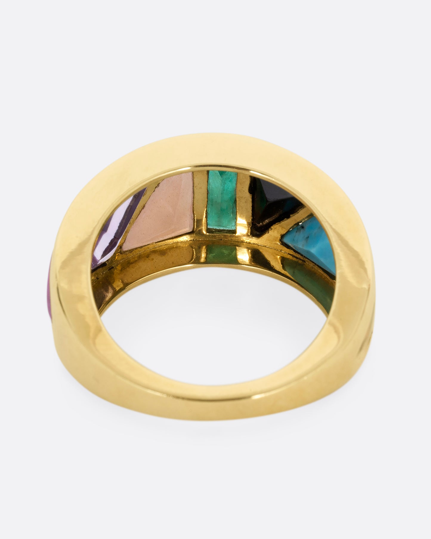 A yellow gold band with an array of gemstones in angular shapes. Shown from the back.